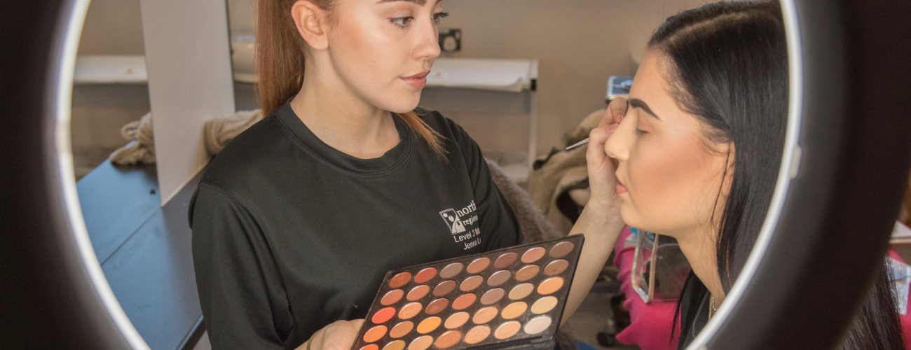 Student applying makeup to model