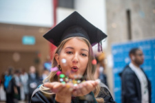 Female Graduate in cap blows glitter towards the camera
