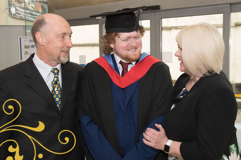 Male Graduate smiling with his parents as they celebrate Graduation together